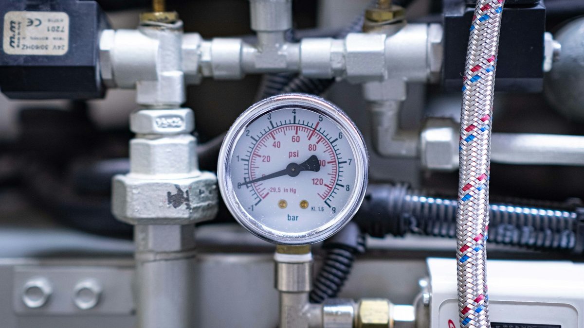 Pressure gauge in psi mounted among threaded fittings on an industrial machine