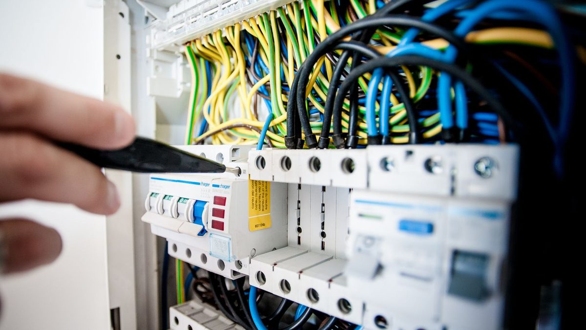 Electrician working inside an open electrical panel with dense point-to-point wiring