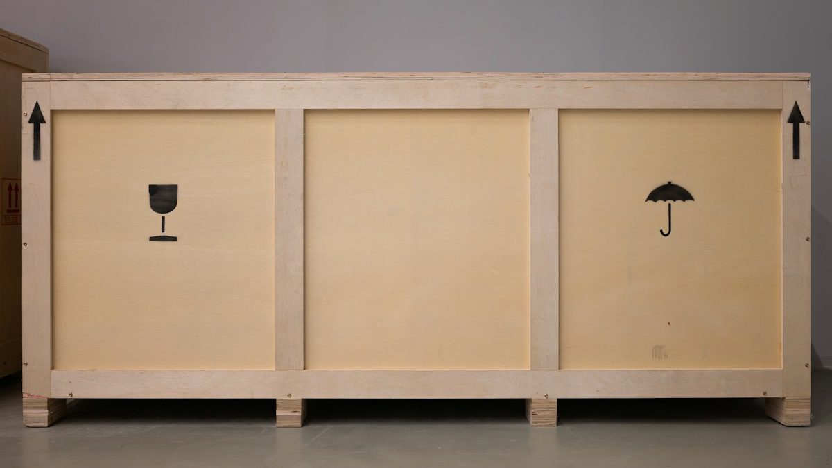 A large plywood shipping crate marked with fragile and keep-dry handling symbols