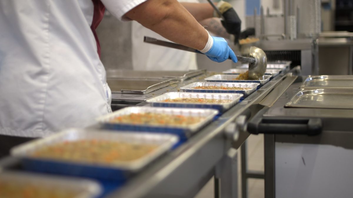 Gloved worker portioning food into trays moving along a production line