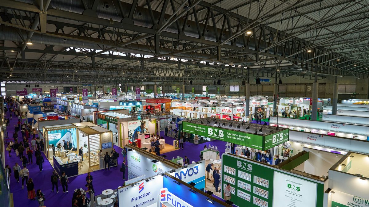 Rows of vendor booths and attendees filling a large trade show exhibition hall