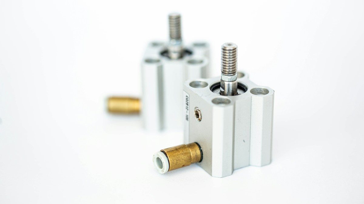 Two compact pneumatic cylinders with push-in fittings on a white surface