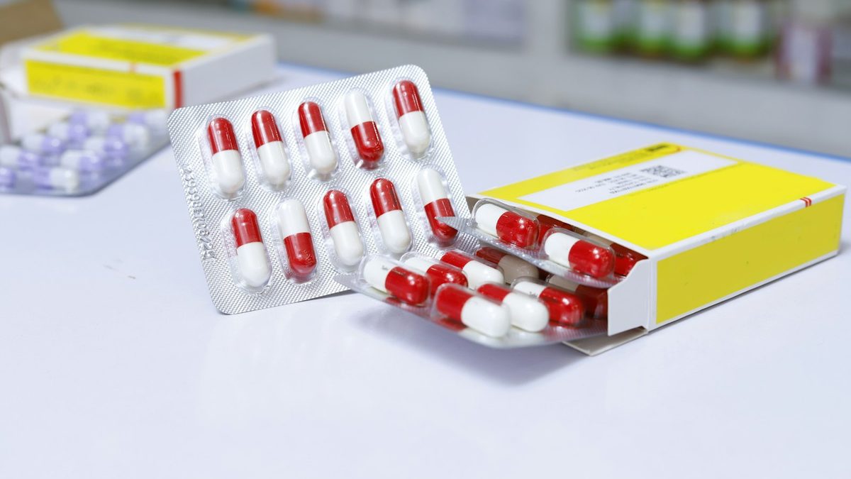 Blister packs of red and white capsules beside a coded pharmaceutical carton on a counter