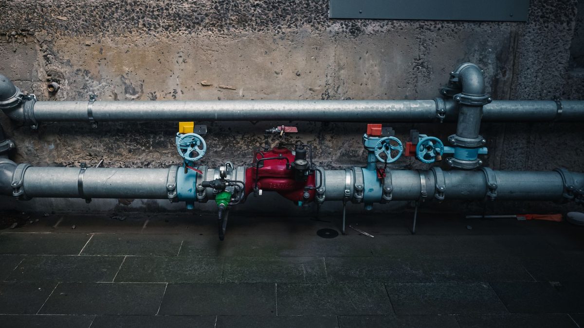 Industrial pipes with multiple colored gate valves mounted against a wall