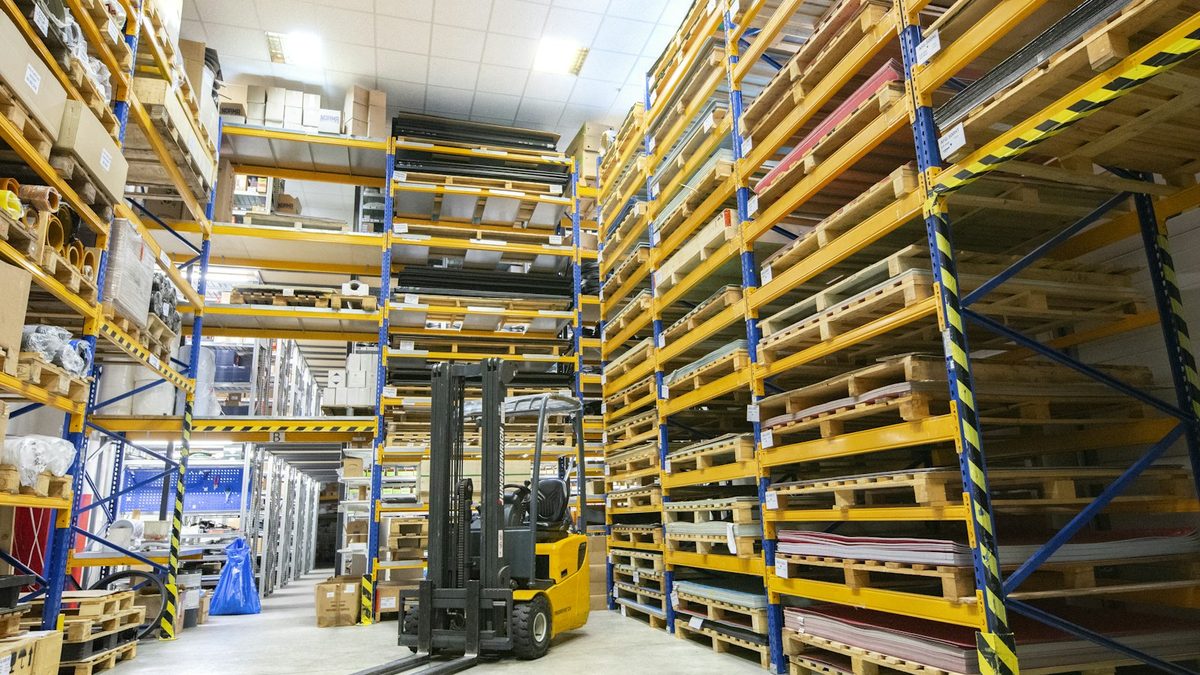 Forklift working an aisle of tall pallet racking in a distribution warehouse